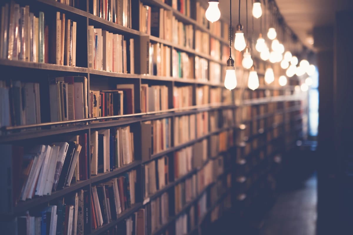 Троє людей (двоє дорослих і одна дитина) читають книги за столом з книжковими полицями на задньому плані
